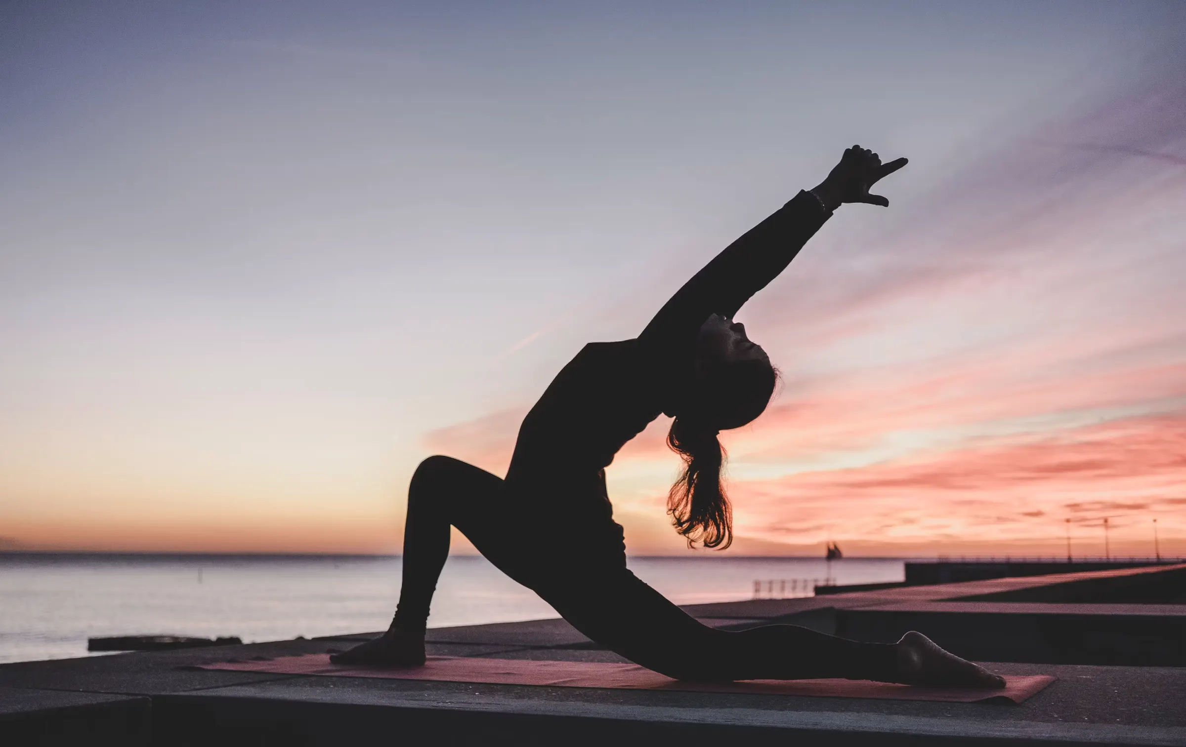 Mujer haciendo yoga frente al mar al atardecer